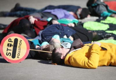 Protesters wearing gas masks staged a “die-in” surrounding a giant neon gas mask banner in George Square ahead of a Glasgow Council Environment Committee meeting on Tuesday 20th March. Image by Ian Macnicol / Friends of the Earth Scotland | Flickr | CC BY 2.0