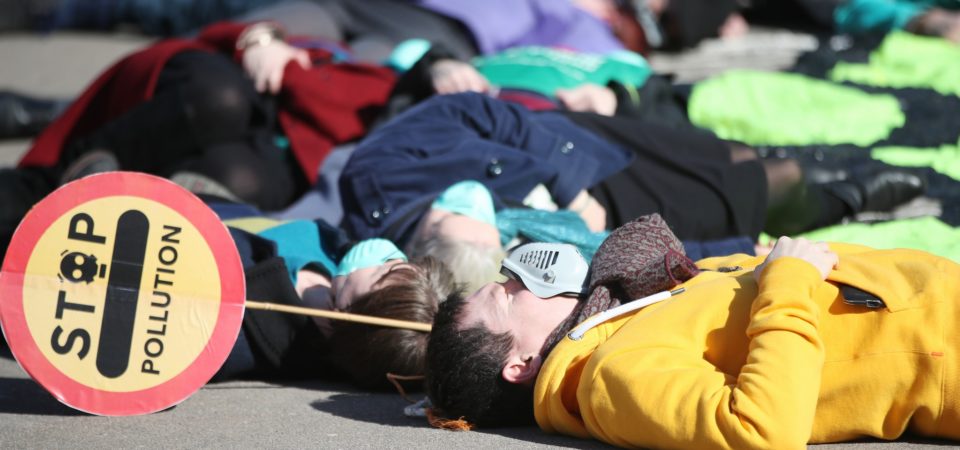 Protesters wearing gas masks staged a “die-in” surrounding a giant neon gas mask banner in George Square ahead of a Glasgow Council Environment Committee meeting on Tuesday 20th March. Image by Ian Macnicol / Friends of the Earth Scotland | Flickr | CC BY 2.0